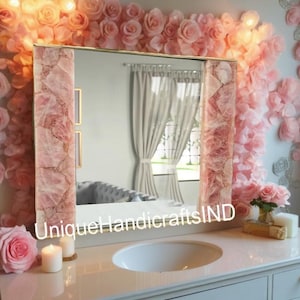May include: A white vanity countertop with a white porcelain sink. The countertop is decorated with two lit candles and a large framed mirror with a pink rose quartz border. The mirror is surrounded by a wall of pink paper flowers.