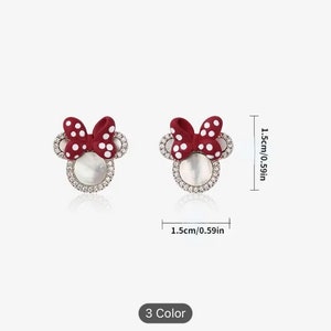 May include: A pair of red and white polka dot bow earrings with a white pearl center and a clear rhinestone halo. The earrings are 1.5 inches in diameter.