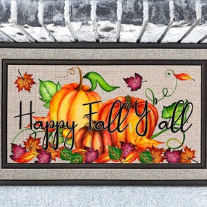 May include: A welcome mat with a burlap background and a brown frame. The mat features a fall-themed design with pumpkins, leaves, and vines. The text "Happy Fall Y'all" is written in black cursive.