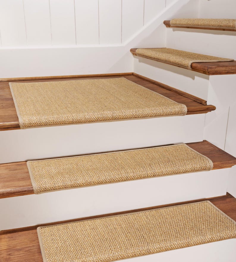 Peut inclure: Marches d'escalier rectangulaires fabriqu&eacute;es dans un mat&eacute;riau en fibres naturelles tiss&eacute;es de couleur beige. Chaque marche pr&eacute;sente un tissage serr&eacute; et textur&eacute;, avec une bordure en tissu beige assortie sur les bords, install&eacute;es sur des marches en bois.