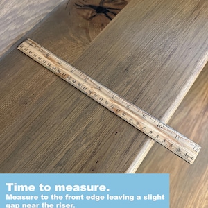 Peut inclure: Une marche d'escalier en bois brun clair avec un grain de bois visible et un n&oelig;ud sombre, plac&eacute;e avec une r&egrave;gle en bois mesurant environ 28 cm. Le texte superpos&eacute; indique : Time to measure. Measure to the front edge leaving a slight gap.