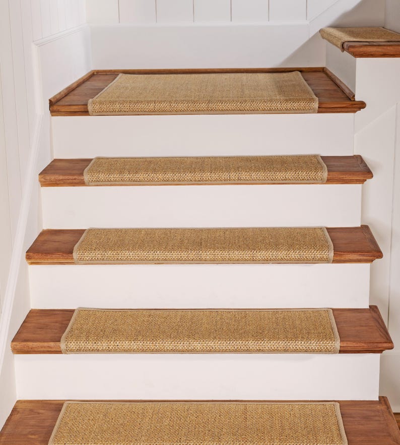 Peut inclure: Un ensemble de marches d'escalier rectangulaires en tissage beige avec des bords finis, install&eacute;es sur un escalier aux marches en bois brun fonc&eacute; et aux contremarches blanches. Les marches textur&eacute;es couvrent chaque marche de l'escalier.