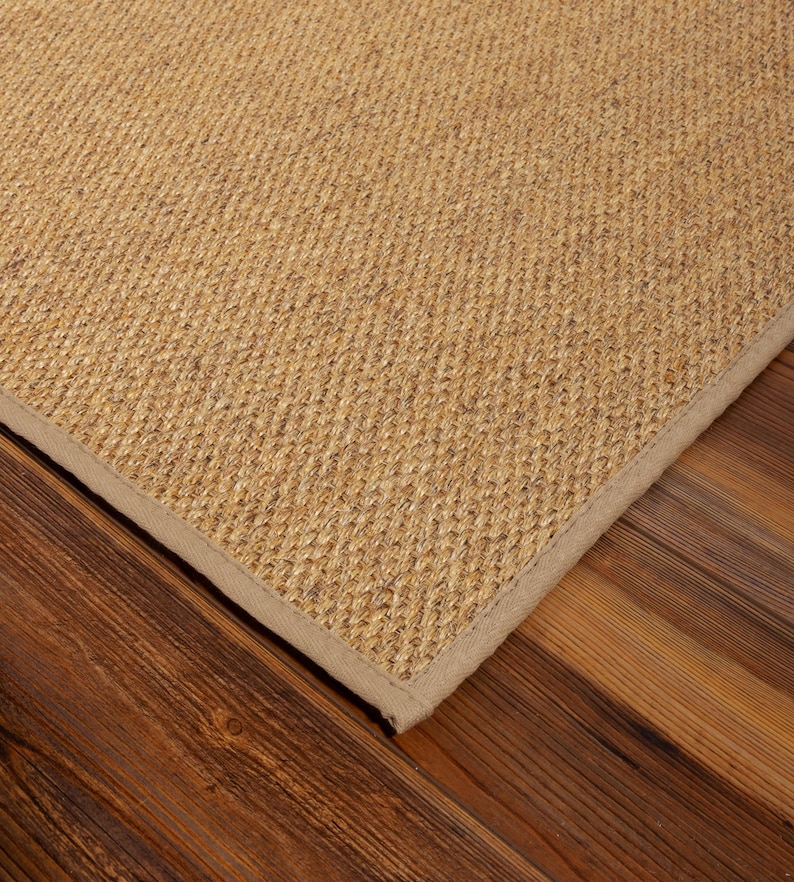 Peut inclure: Un tapis rectangulaire pr&eacute;sentant une texture en fibres naturelles de couleur beige avec un tissage serr&eacute; et r&eacute;gulier. Le tapis est dot&eacute; d'une bordure en tissu assorti de couleur beige clair qui longe le bord droit et net du mat&eacute;riau.