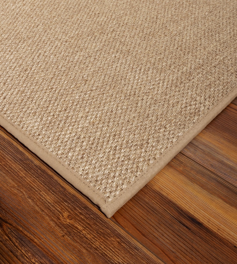Peut inclure: Un tapis rectangulaire compos&eacute; d'un tissage serr&eacute; en fibres naturelles de couleur beige, pr&eacute;sentant une texture uniforme. Le tapis est bord&eacute; d'une finition en tissu assorti qui longe le bord droit et net de l'ensemble de la pi&egrave;ce.