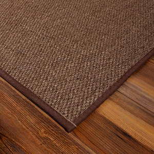 Peut inclure: Un tapis rectangulaire pr&eacute;sentant une surface tiss&eacute;e brune textur&eacute;e avec un motif en grille serr&eacute; et uniforme. Le tapis est fini avec une bordure en tissu marron fonc&eacute;, lisse et solide, qui longe le bord, offrant un cadre net et d&eacute;fini.