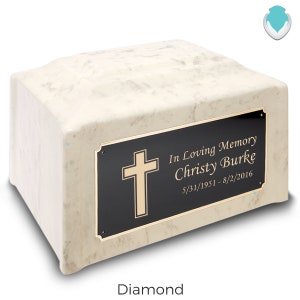 May include: White marble cremation urn with a gold cross and a black plaque that reads "In Loving Memory Christy Burke 5/31/1951 - 8/2/2016".