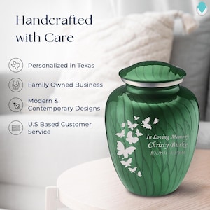 May include: Green metal cremation urn with a swirl design and a silver lid. The urn has a white butterfly design and the text "In Loving Memory Christy Burke 5/31/1951-8/2/2016".