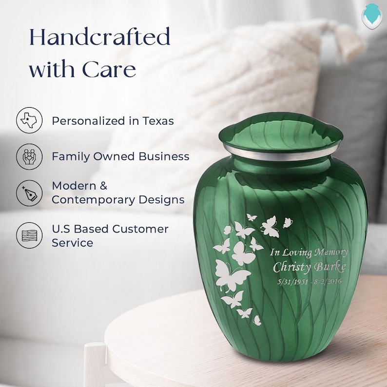 May include: Green metal cremation urn with a swirl design and a silver lid. The urn has a white butterfly design and the text "In Loving Memory Christy Burke 5/31/1951-8/2/2016".