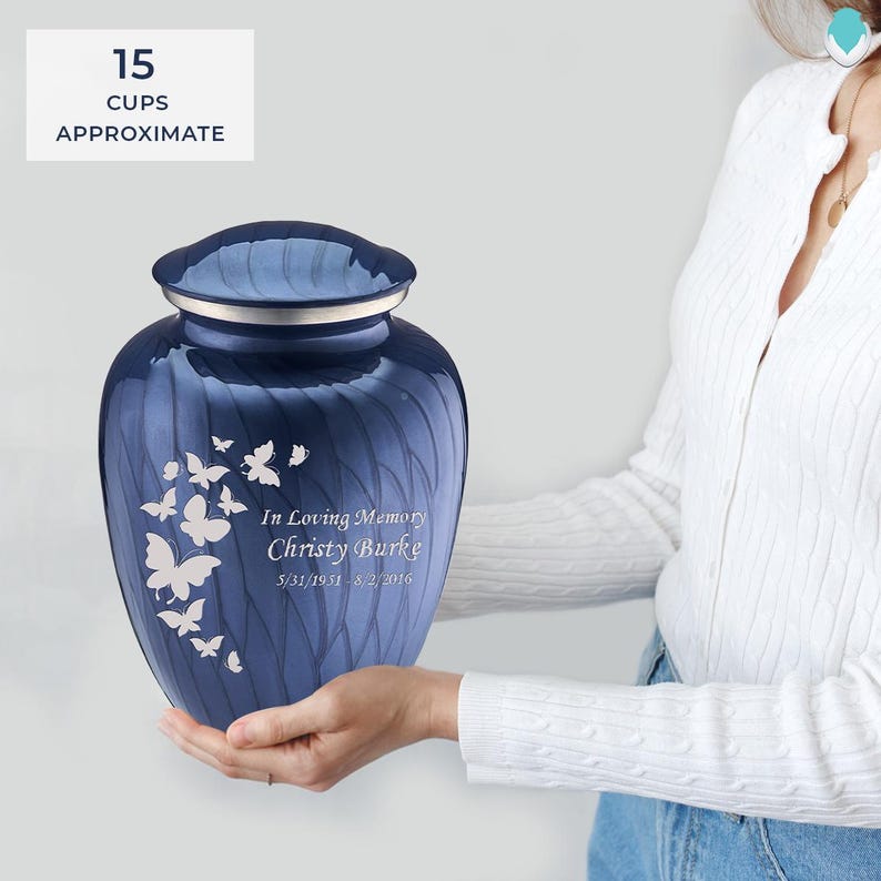 May include: A blue cremation urn with a swirl pattern and silver accents. The urn features a butterfly design and the inscription "In Loving Memory Christy Burke 5/31/1951-8/2/2016".