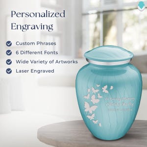 May include: A light blue cremation urn with a silver lid and a silver butterfly design. The urn is engraved with the text "In Loving Memory Christy Burke 5/31/1955 - 1/2/2016".