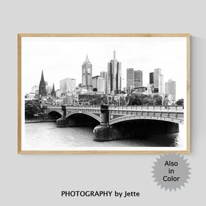 May include: Black and white photograph of a city skyline with a bridge in the foreground. The city skyline features tall buildings and a river. The bridge is a stone arch bridge with a road running over it. The photograph is framed in a wooden frame.