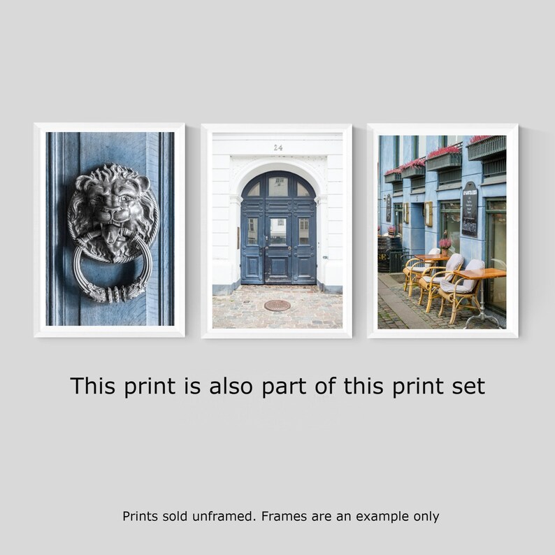 May include: A set of three framed prints featuring architectural details in a European city. The first print shows a close-up of a silver lion door knocker on a blue door. The second print shows a blue door with a white frame and the number 24 above it. The third print shows a street scene with blue buildings and tables and chairs set up outside a cafe.