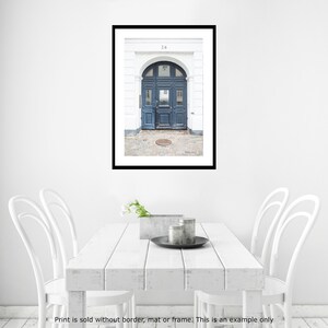 May include: A photograph of a blue door with a white frame and a white building behind it. The door has a rounded archway and a metal door handle. The number 24 is visible above the door.