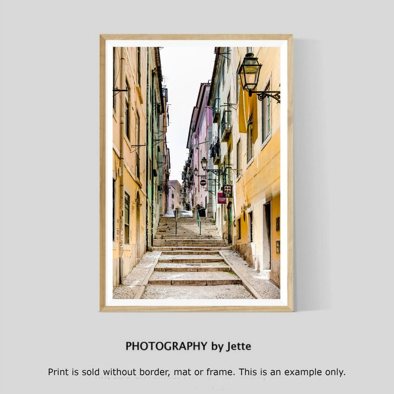 May include: A narrow, cobblestone street in a European city with colorful buildings on either side. The street leads up a set of stairs to a bright, sunny area.