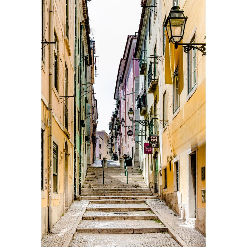 May include: A narrow, cobblestone street in a European city with colorful buildings on either side. The street leads up a set of stairs.