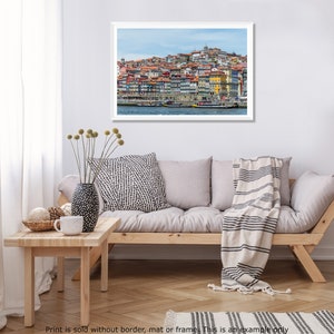 May include: A colorful cityscape with a hillside of buildings overlooking a river with boats. The buildings are a mix of red, orange, yellow, and white.
