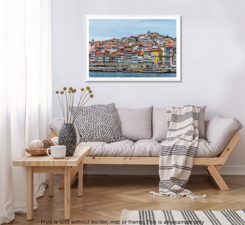 May include: A colorful cityscape with a hillside of buildings overlooking a river with boats. The buildings are a mix of red, orange, yellow, and white.