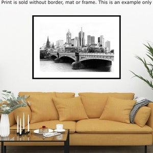 May include: Black and white photograph of a city skyline with a bridge in the foreground. The bridge has multiple arches and is made of stone. The city skyline is in the background and includes tall buildings. The photo is framed in a black frame.