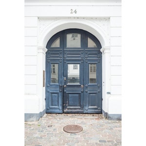May include: A blue wooden door with a decorative archway and the number 24 above it. The door has multiple panels and is set in a white wall.