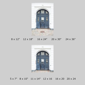 May include: A close-up of a dark blue wooden door with a decorative archway and white trim. The door has a small window in the center and a metal door handle. The door is set against a white brick wall.