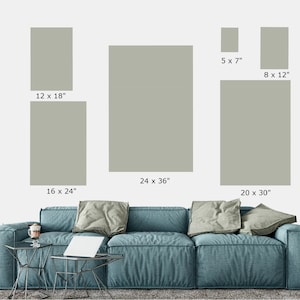 May include: Five different sizes of framed artwork with a light gray background. The frames are all the same color and style. The artwork is displayed on a white wall above a blue sofa.