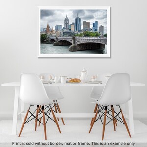 May include: A photograph of a city skyline with a bridge in the foreground. The city is in the distance and the bridge is in the foreground. The sky is cloudy and the water is calm.