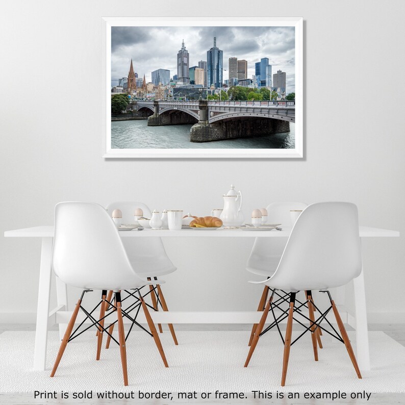 May include: A photograph of a city skyline with a bridge in the foreground. The city is in the distance and the bridge is in the foreground. The sky is cloudy and the water is calm.