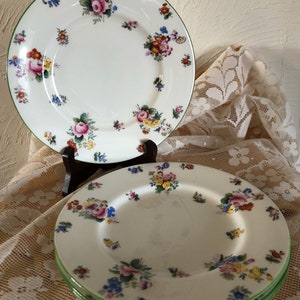 May include: Three white ceramic plates with a green rim and a floral pattern in shades of pink, yellow, blue, and green.