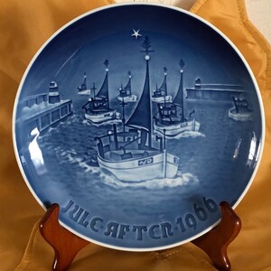 May include: Blue and white Christmas plate with a scene of fishing boats sailing into a harbor with a star on top of a Christmas tree. The plate reads "Juleaften 1966".
