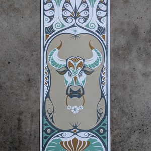 May include: A stylized illustration of the Taurus zodiac sign, featuring a bull's head with a floral nose ring. The bull is surrounded by intricate floral patterns in shades of green, gold, and brown. The text "Taurus" is printed at the bottom of the image.
