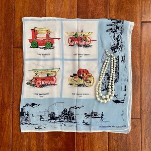 May include: A blue and white vintage silk scarf with a print of four antique fire engines. The scarf features the names "The Hasseed", "The White Ghost", "The Blue Boys", and "The White Turtle" with their corresponding years. A pearl necklace is draped over the scarf.
