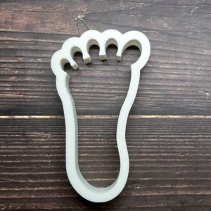 May include: White plastic cookie cutter shaped like a human foot.