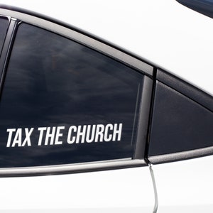 May include: A white car window with a black frame and a sticker that reads "TAX THE CHURCH" in white capital letters. The sticker is centered on the window, and the car's body is white.