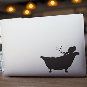 May include: A black silhouette of a person in a bathtub blowing bubbles on a silver laptop.