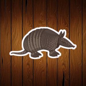 May include: A cartoon illustration of an armadillo with a white border. The armadillo is primarily brown with a segmented shell and a dotted pattern on its body. It has a long snout and small ears, set against a wooden background.
