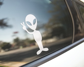 May include: A white alien sticker with a peace sign on a car window.
