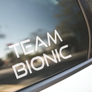May include: A white car window with a white vinyl sticker that says "TEAM BIONIC".