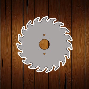May include: A silver saw blade with white teeth and a brown center hole. The blade is against a brown wood background.