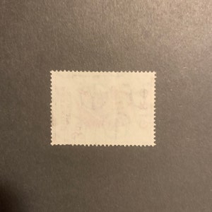 May include: A white postage stamp with a red and blue design. The stamp has a serrated edge and is slightly worn.