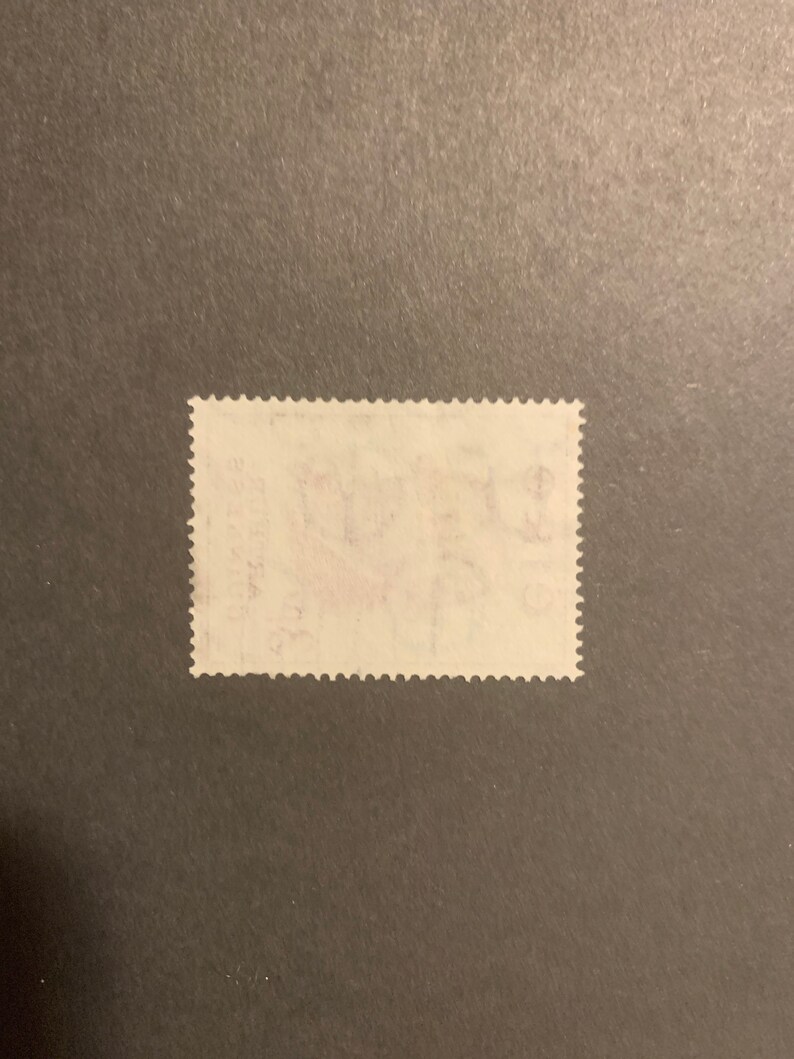 May include: A white postage stamp with a red and blue design. The stamp has a serrated edge and is slightly worn.