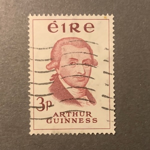 May include: A vintage Irish postage stamp featuring a portrait of Arthur Guinness, the founder of the famous brewery. The stamp is red and white and has the text "&eacute;ire" and "3p ARTHUR GUINNESS" printed on it.