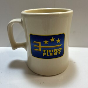 May include: White ceramic mug with a blue and yellow logo that says "Third Fleet" with three stars above the text.