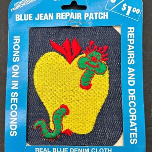 May include: A blue jean repair patch with a yellow apple and a green worm embroidered on it. The patch is 4 inches by 5 inches and is made of real blue denim cloth. The packaging says "Giant 4" x 5" Size", "Blue Jean Repair Patch", "Genuine Embroidered", "Irons on in Seconds", "Repairs and Decorates", and "Real Blue Denim Cloth".