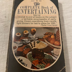 May include: The Complete Book of Entertaining by Nata Lee, a cookbook with a black cover and a photo of a dinner table setting with food and drinks. The book cover text reads "A book to end all books on the subject... a veritable encyclopedia of party-giving. Covers everything from candle-light dinners for two to galas for 200." -Dallas Times Herald