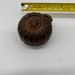 May include: A dark brown, antique-style bottle stopper with a bee emblem. The stopper is approximately 2 inches in diameter. The stopper has a ribbed design around the sides.