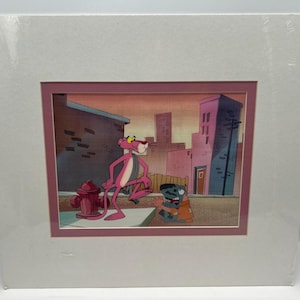 May include: A framed animation cel featuring the Pink Panther and a small, dark-colored character. The Pink Panther, in his signature pink hue, stands near a red fire hydrant. The background depicts a city scene with buildings and a sunset.
