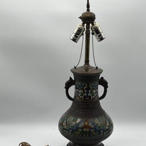 May include: A vintage cloisonné table lamp with a dark brown base and a green, blue, and gold cloisonné design. The lamp has two light sockets and a chain hanging from the top.