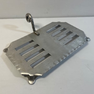 May include: A silver metal toast rack with a handle. The rack has a rectangular shape with a series of slots for holding toast.