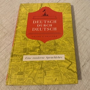 May include: A red and yellow book cover with the title "Deutsch durch Deutsch" and the author "Franz J. Pfister". The cover features a map of Berlin with various landmarks and street names.