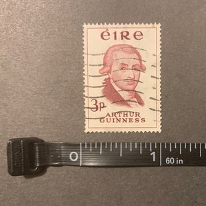May include: A vintage Irish postage stamp featuring a portrait of Arthur Guinness, the founder of the Guinness brewery. The stamp is red and white and has the text "&eacute;ire" and "3p ARTHUR GUINNESS" printed on it.